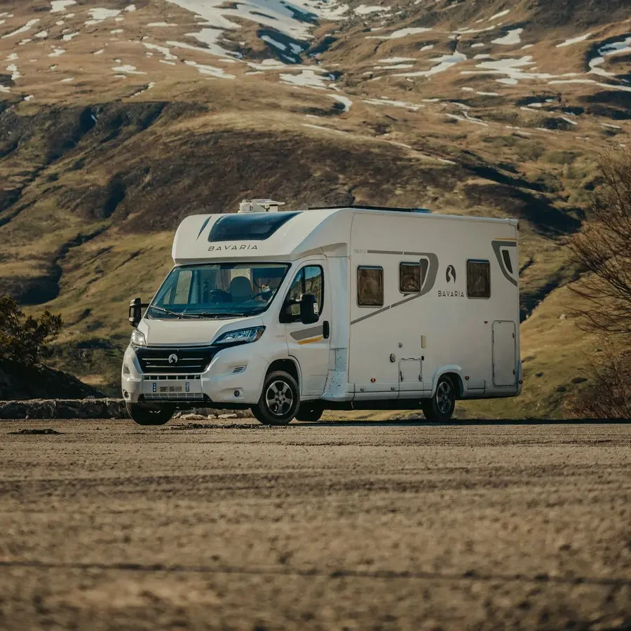 Un camper bianco con cabina e cellula abitativa parcheggiato davanti alle montagne